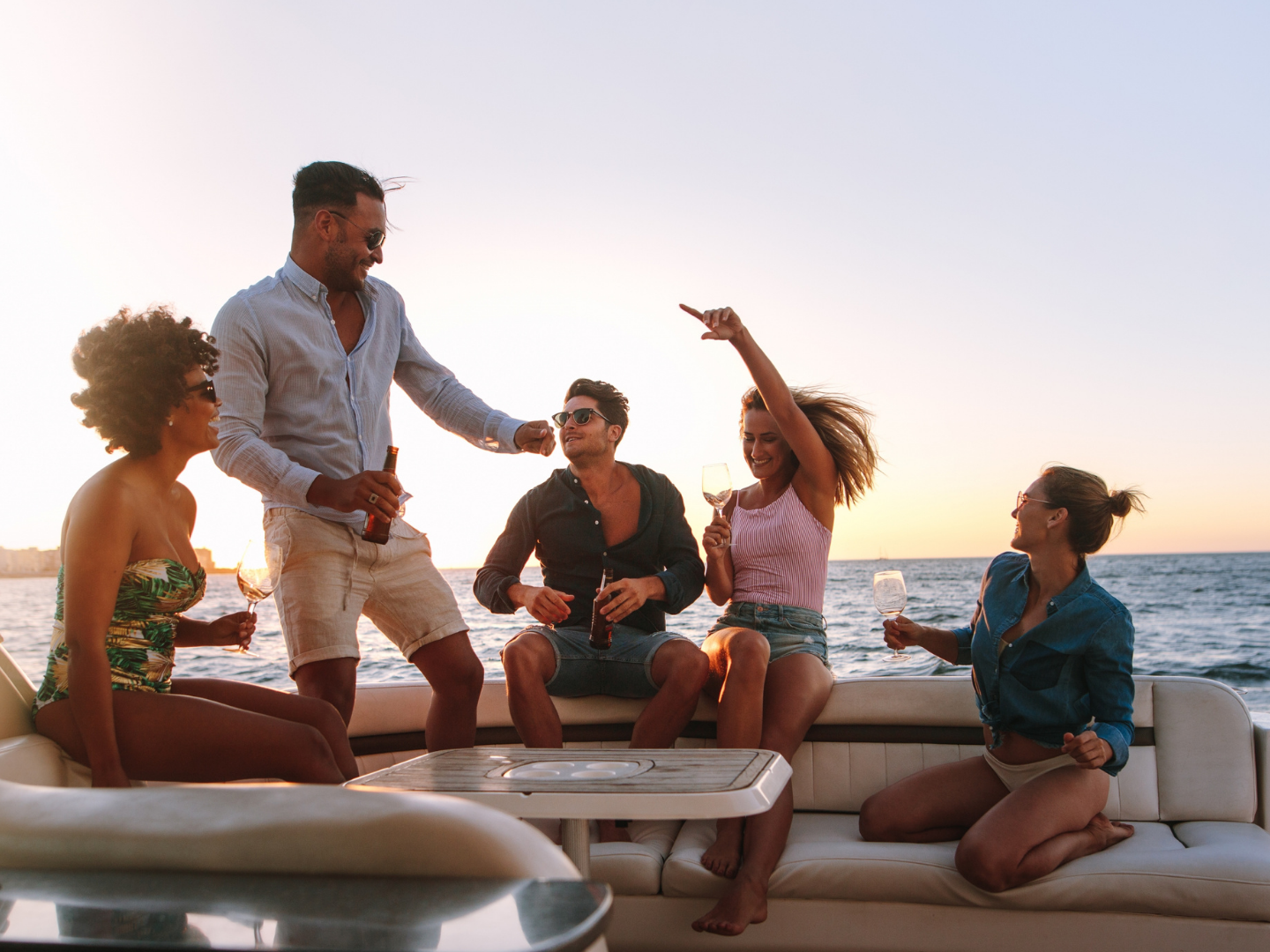 Group of people enjoying drinks and dancing on a boat at sunset.