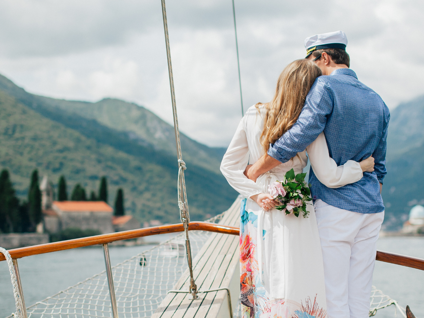 Couple embracing on a boat, surrounded by scenic mountains and water.