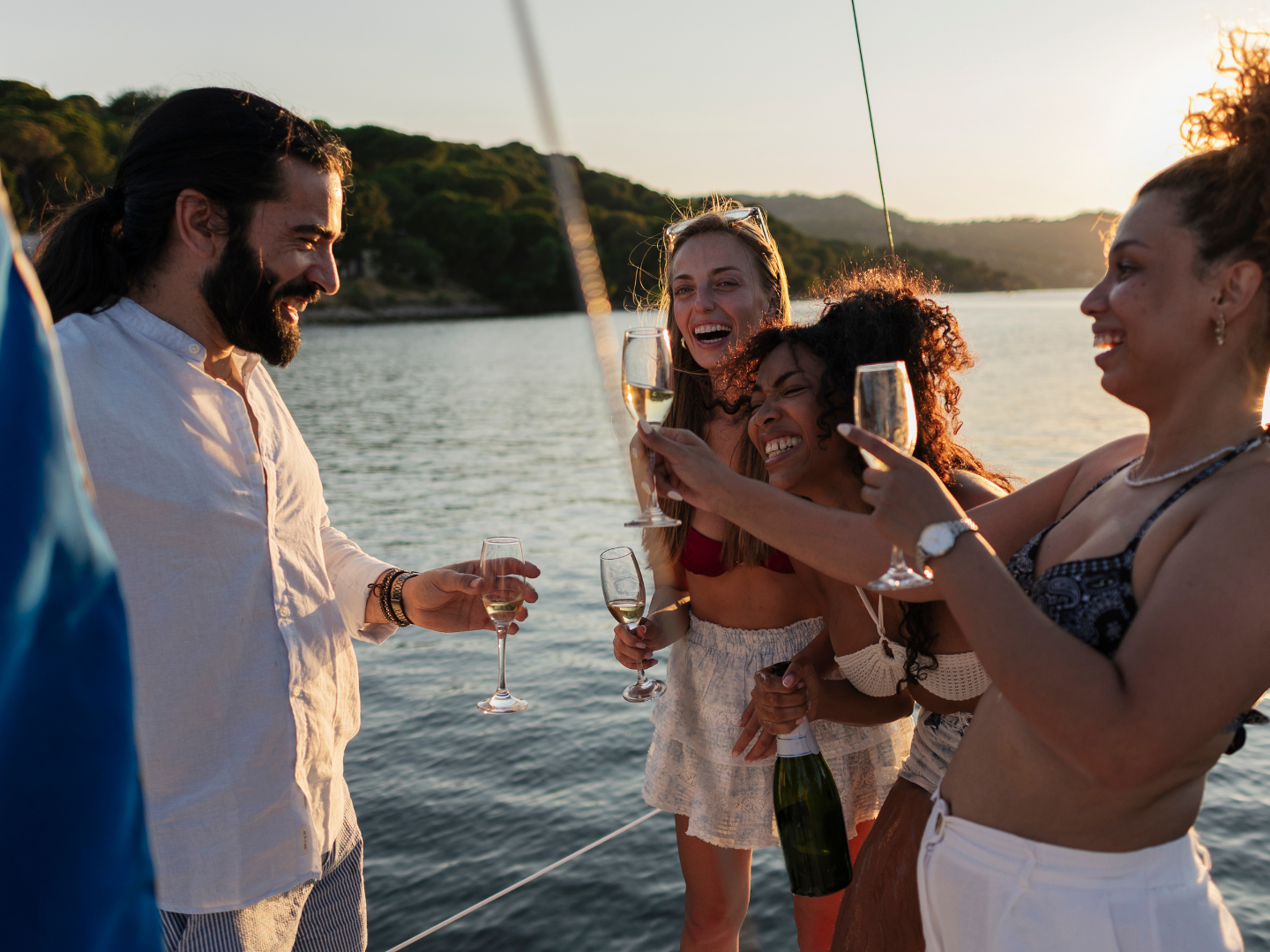 Group of friends celebrating with drinks on a sailboat at sunset.