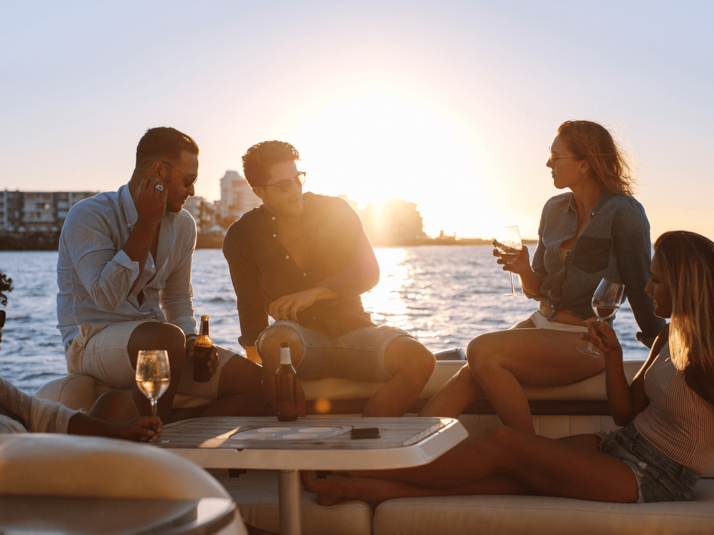 Group of people relaxing with drinks on a boat at sunset.