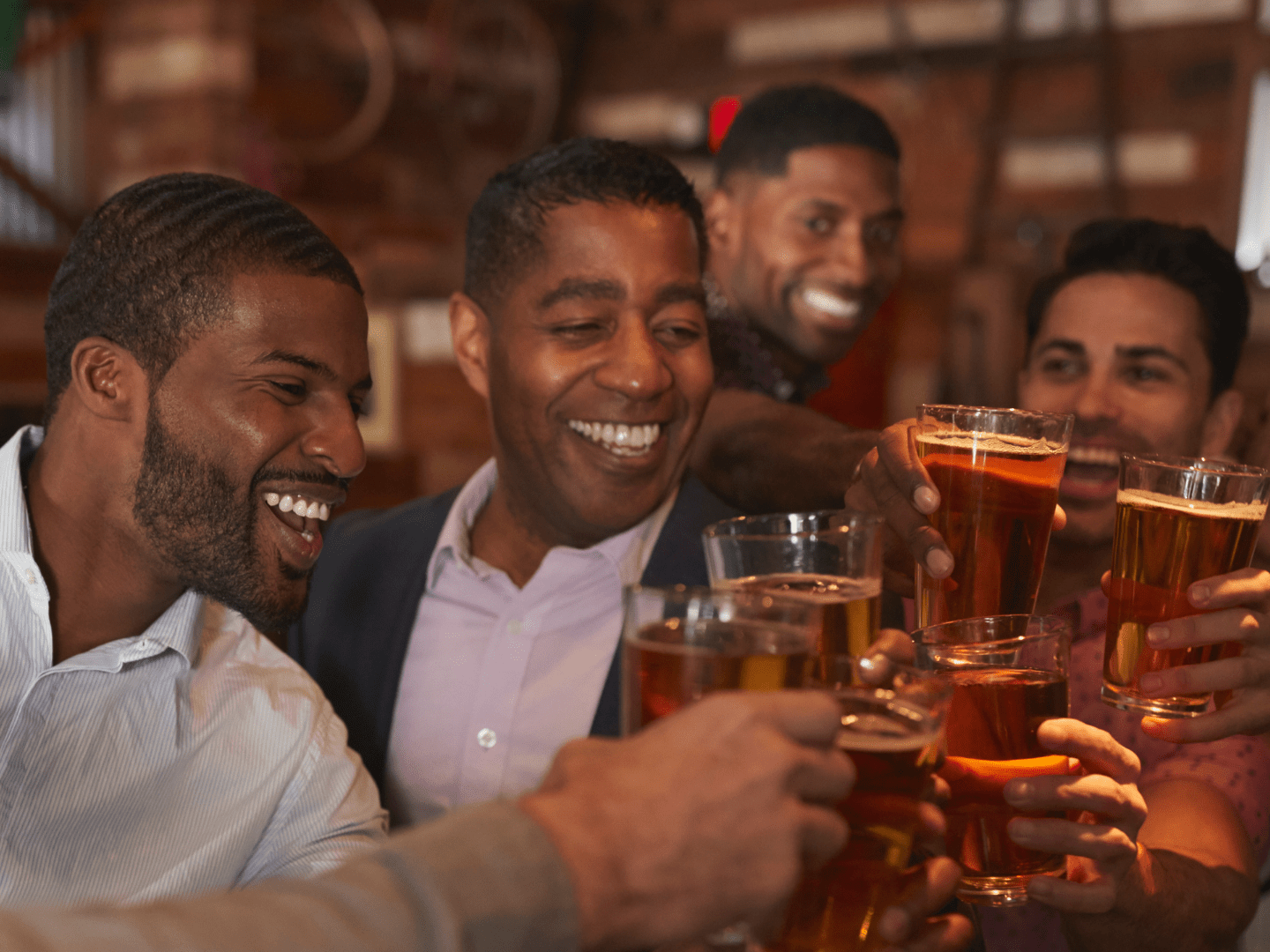 Group of men smiling and toasting with beer glasses in a bar setting.