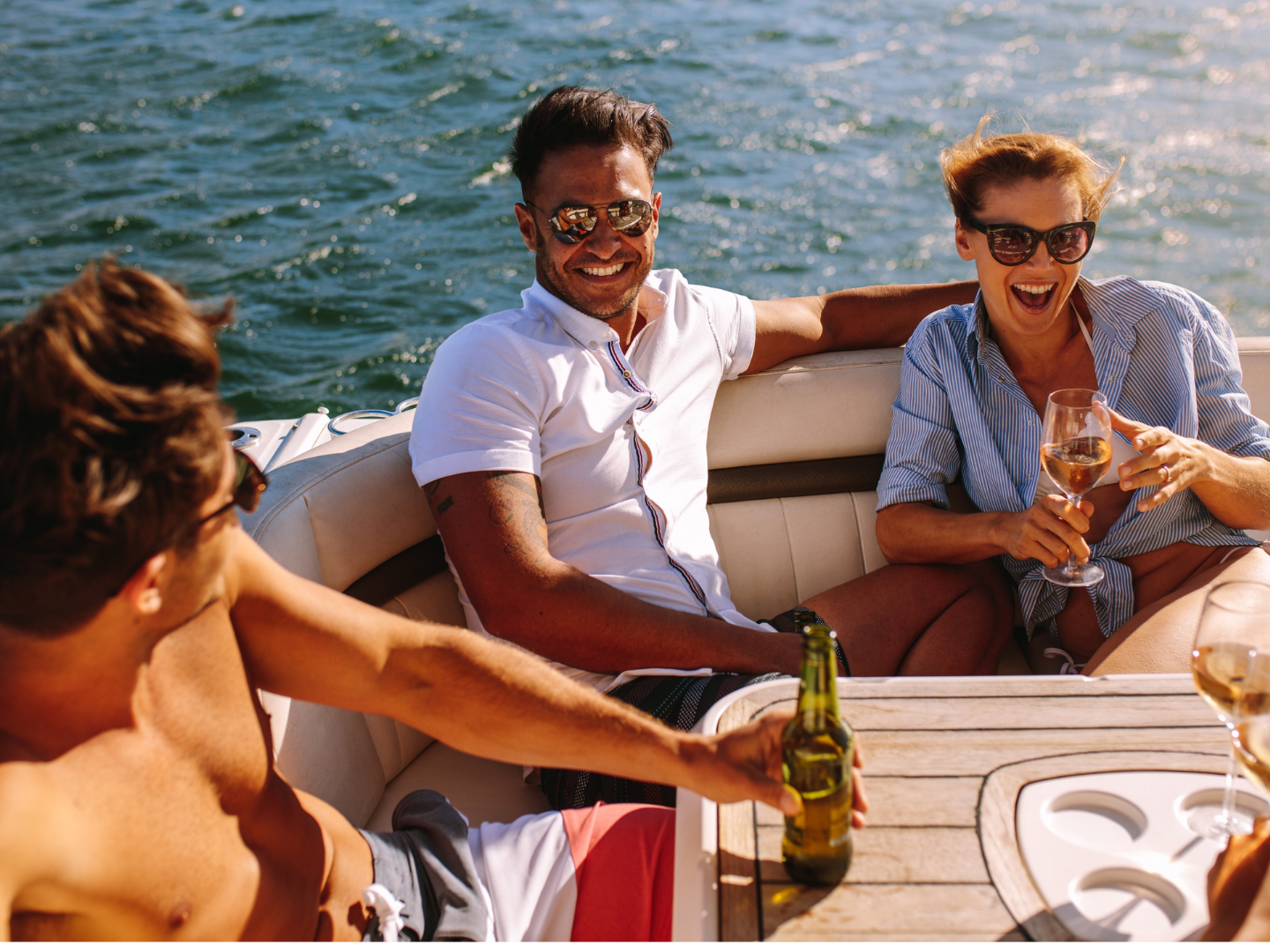 Group of friends laughing and relaxing with drinks on a boat in the sun.