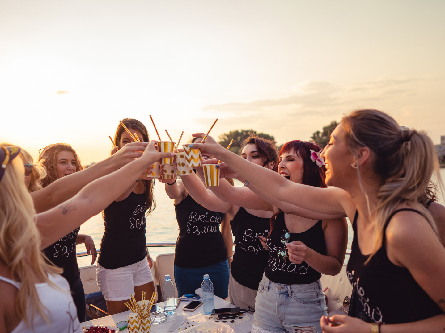 Group of women on a boat toasting with drinks at sunset.