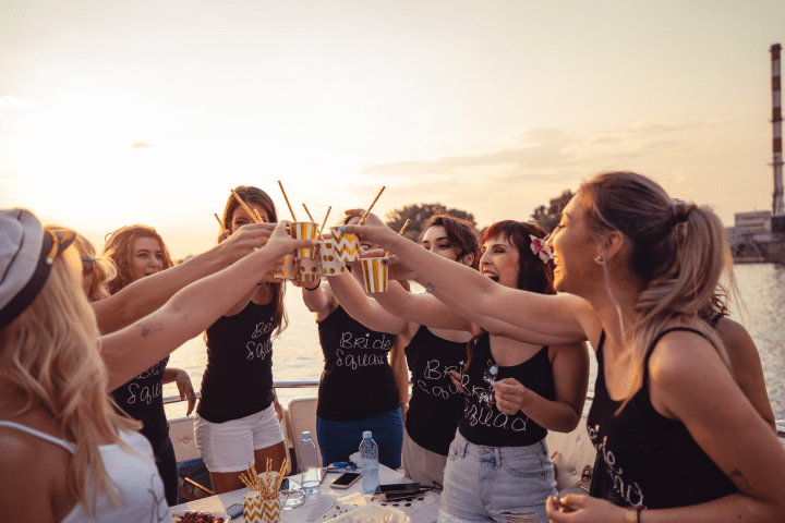 Group of women on a boat toasting with drinks at sunset.