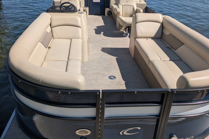 Pontoon boat with beige seating docked on a lake.