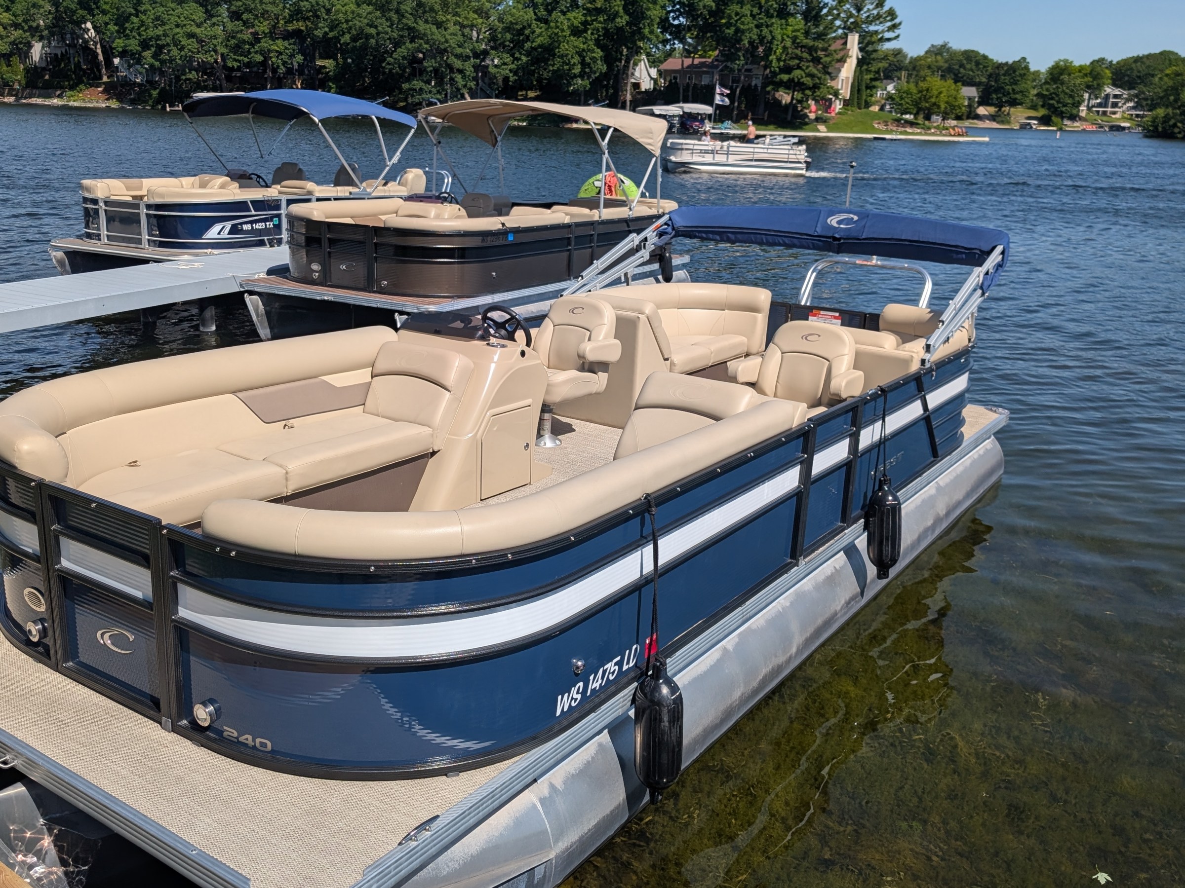 Blue and beige pontoon boat docked on a lake.