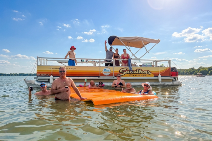 People enjoying a day on a pontoon boat and swimming with an orange float in the water.