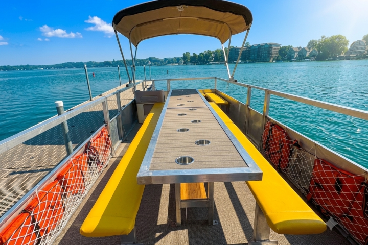 Boat deck with canopy, long table, yellow benches, surrounded by water.